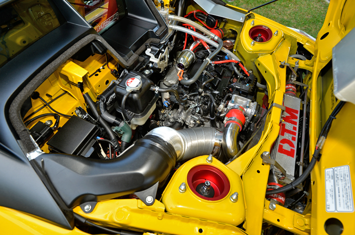 エンジンの後方に鎮座する大型インタークーラー。効率を求めたパイプレイアウトのため、ボディを一部カットし、リヤフェンダー内部にパイピングを通しました。
インタークーラー後方には大型電動ファンを設置し、冷卸効率を向上させています。純正エアダクトを延長し、外気をダイレクトにインタークーラーコアへ導風しています。